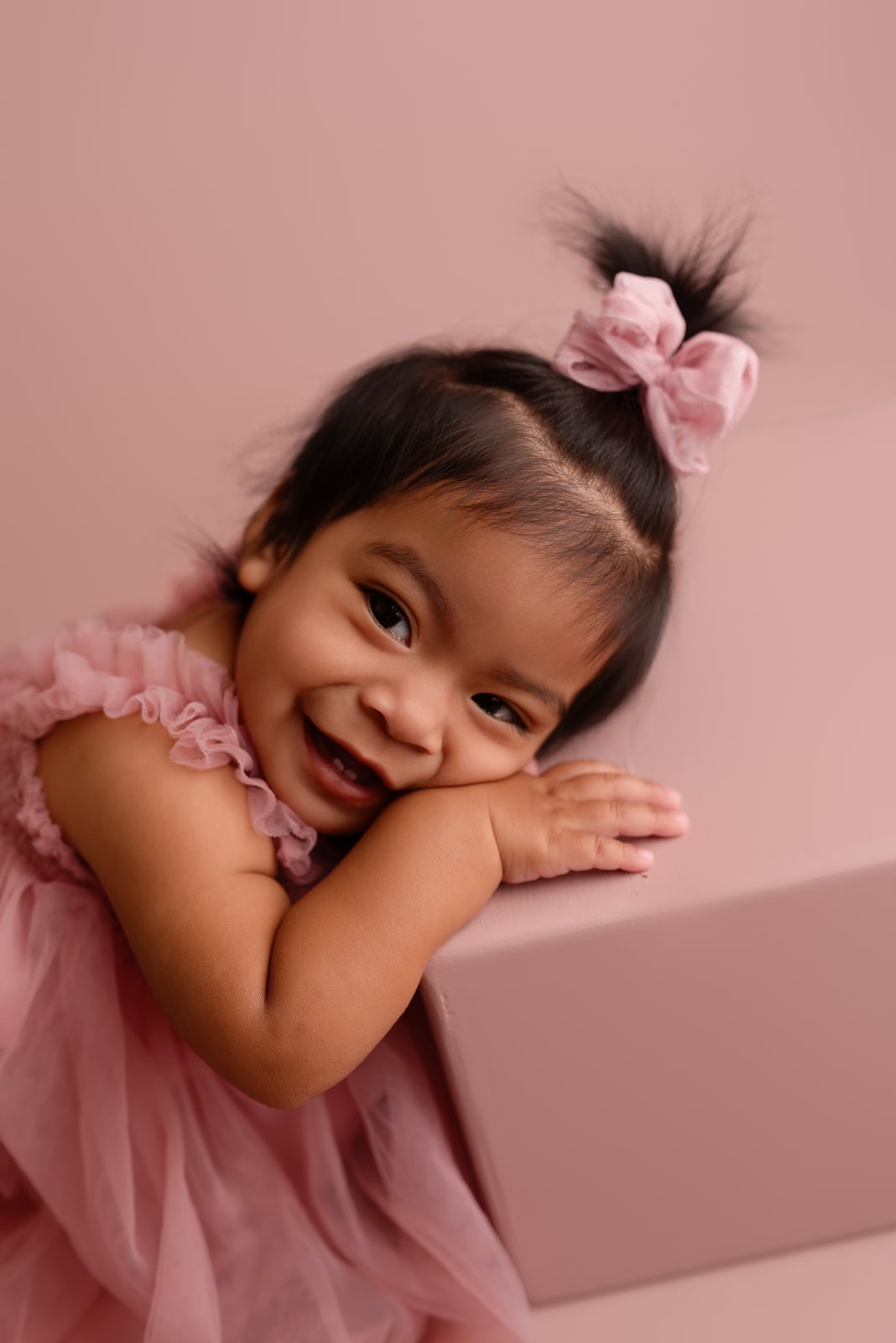 Toddler in a pink tulle dress with a bow, leaning on a prop box