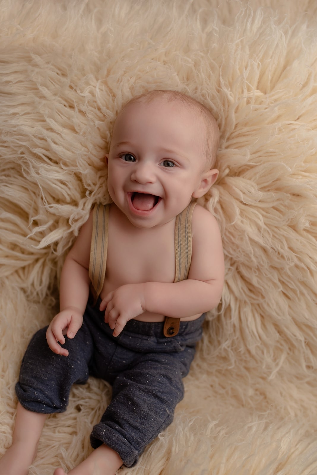 Baby laughing on a cream fur rug in overalls
