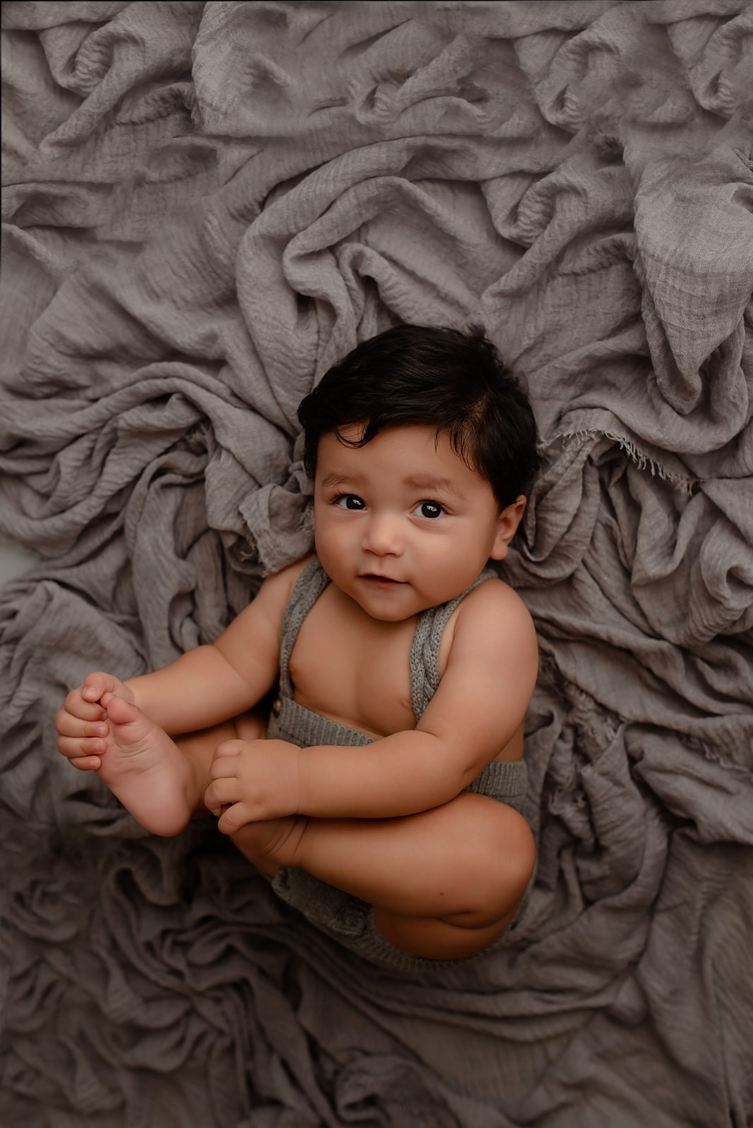 Baby sitting cross-legged on a grey textured rug