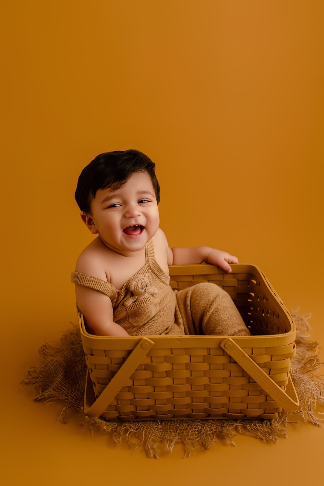 Baby sitting in a woven basket against a mustard backdrop