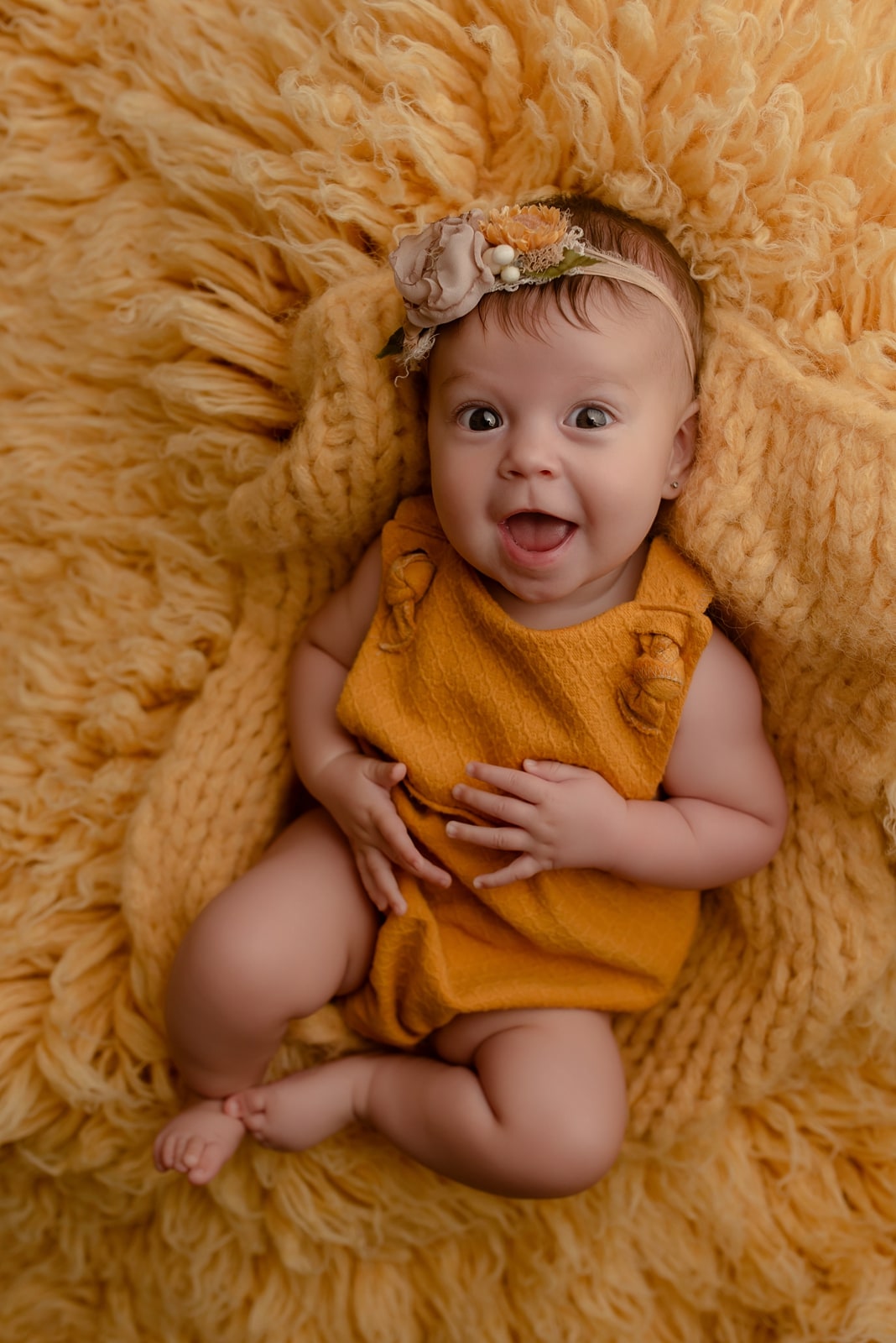 Baby in a floral headband on a mustard fur rug