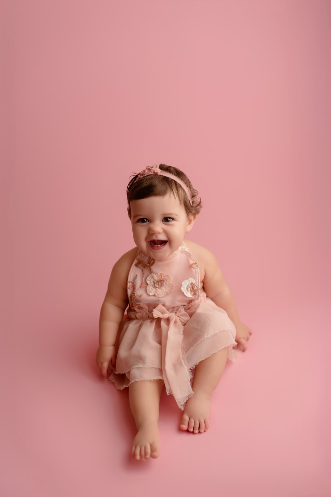 Baby in a floral dress against a pink backdrop