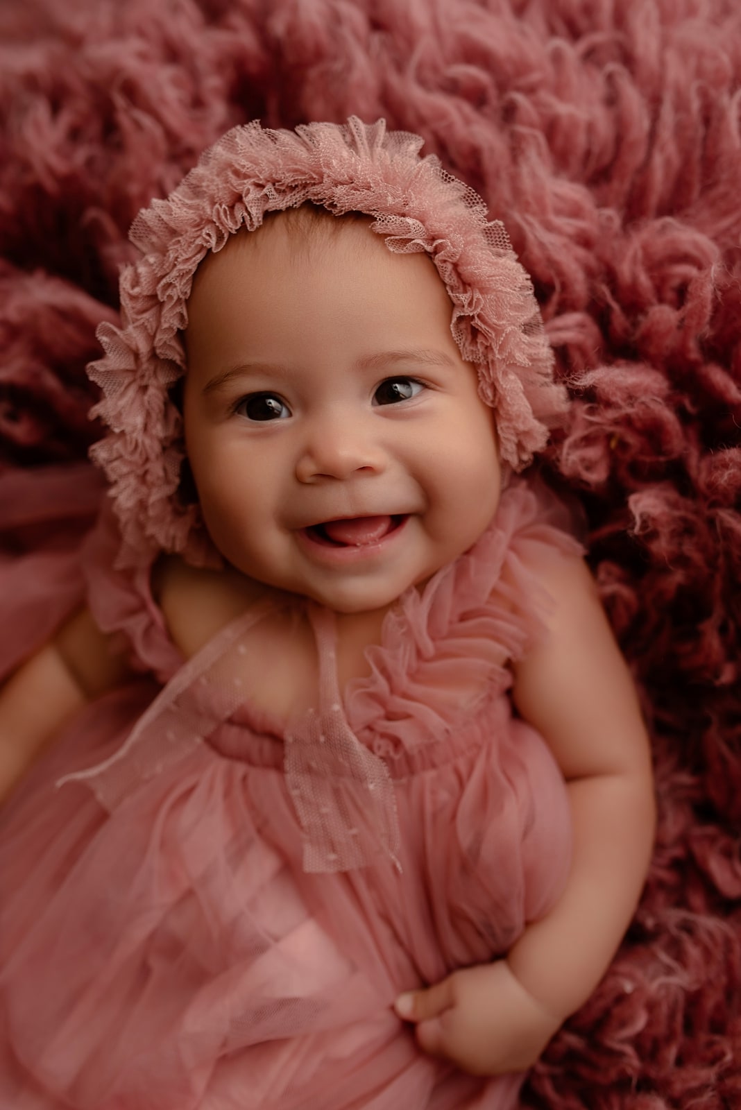 Baby in a pink bonnet on a pink fur rug