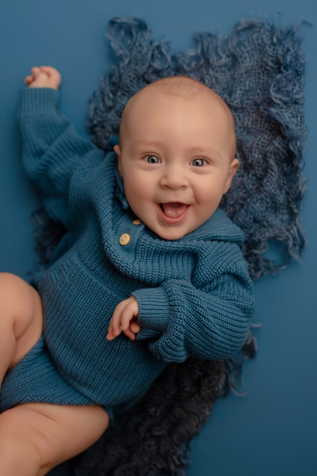 Baby in a teal knit sweater laughing on a dark blue rug